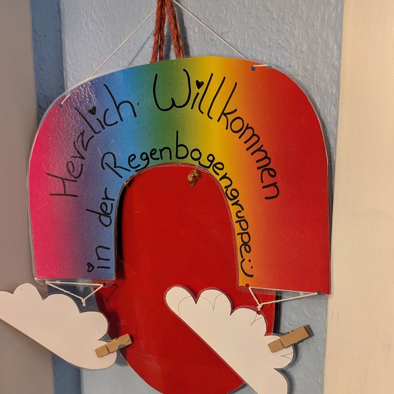Selbst gebasteltes Schild in Regenbogenfarben: „Herzlich Willkommen in der Regenbogengruppe“