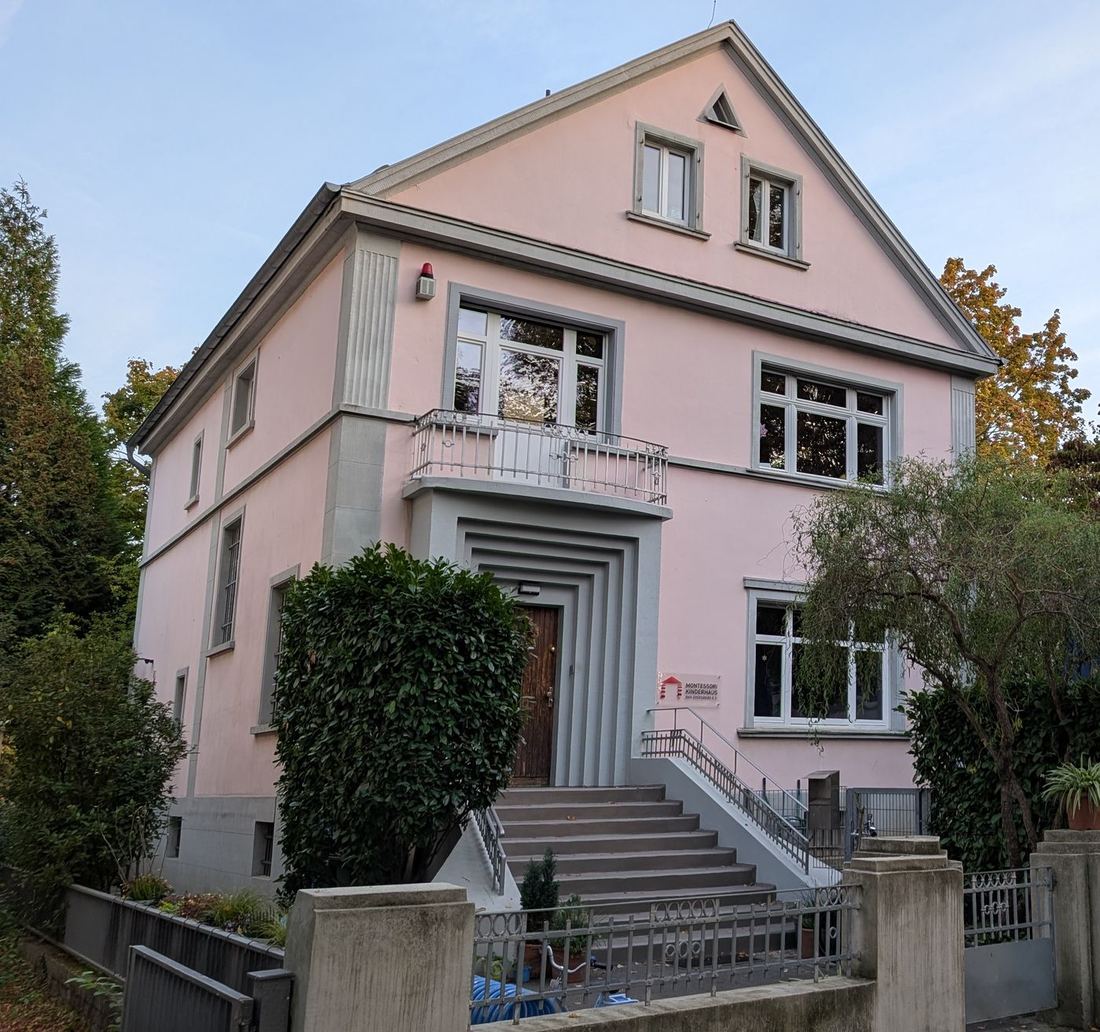 Die rosa Villa des Kinderhauses von der Straße aus, mit Eingangstreppe und Moki-Schild